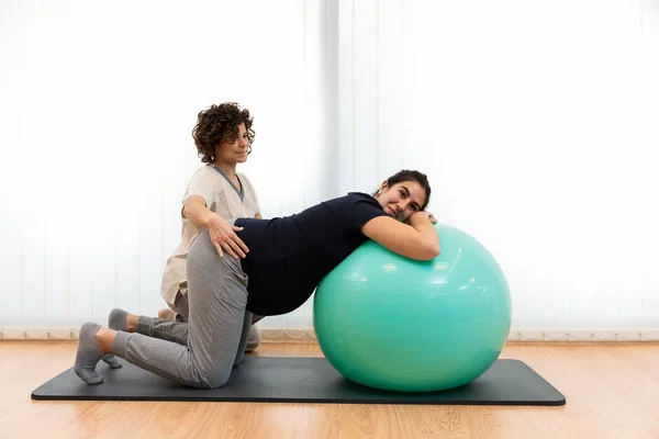 Hamile bir kadın fizyoterapistinin yardımıyla nefes egzersizleri yapıyor ve bir fitness topunun üzerinde dinleniyor. — Stok fotoğraf