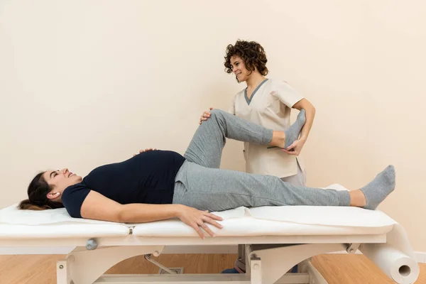 A pregnant woman lying on a massage table while a physiotherapist massages her legs at a health center — Stock Photo, Image