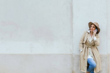 Şık, kalın elbiseli bir kadın sokakta dikilirken telefonla konuşuyor..