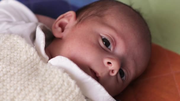 Közelkép egy újszülött babáról, aki a kamerába néz, miközben a hátán fekszik az ágyon.. — Stock videók