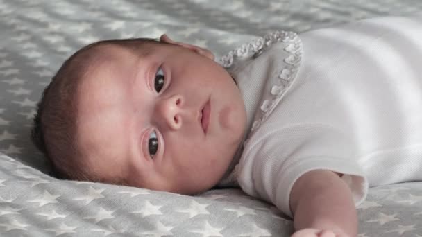 Piccolo neonato che guarda la macchina fotografica sdraiato sulla schiena su un comodo letto. — Video Stock