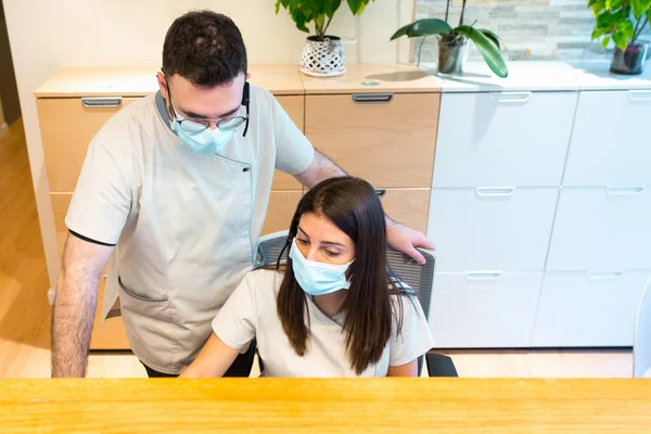 Bir sağlık merkezinin resepsiyonunda çalışan kadın ve erkek resepsiyonistler yüz maskesi kullanıyorlar.. — Stok fotoğraf