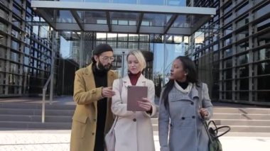 İş arkadaşları dijital tablet kullanıyorlar ve ofis binası dışında birlikte yürürken iş projelerini tartışıyorlar..