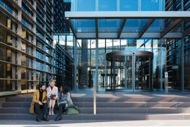 Profesyonel iş arkadaşları ofis binasının dışındaki merdivenlerde otururken yeni projeleri tartışıyor..