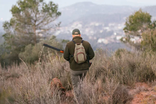 Jäger mit Schrotflinte und Hund neben ihm beim Gassigehen durch die Berge — Stockfoto