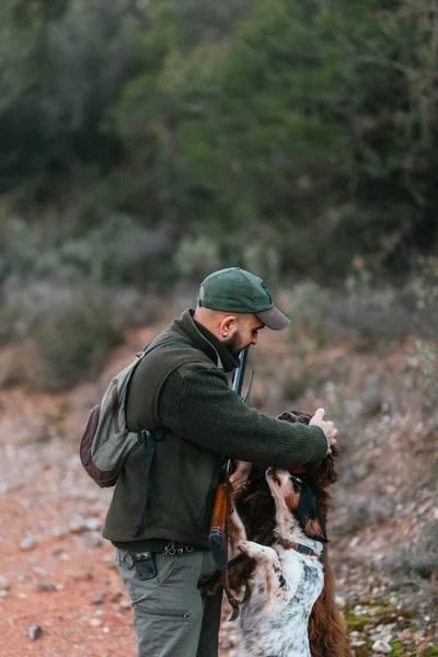 Jäger mit seiner Schrotflinte streichelt seine beiden Hunde in den Bergen — Stockfoto