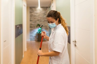 Temizlikçi kadın spa ya da sağlık merkezinin koridorunu temizlerken yüz maskesi kullanıyor..
