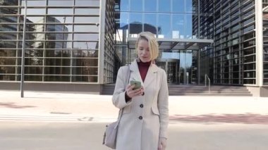 İş kadını ofisten çıktıktan sonra sokakta yürürken cep telefonunu kullanıyor ve gülümsüyor..