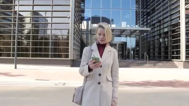 Geschäftsfrau benutzt ihr Handy und lächelt, während sie nach dem Verlassen des Büros die Straße hinuntergeht. — Stockvideo