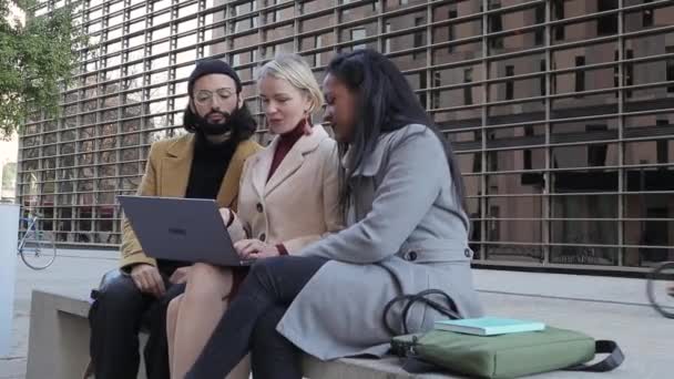 Коллеги, используя ноутбук, обсуждают новые рабочие проекты и делятся идеями, сидя на скамейке на открытом воздухе. — стоковое видео