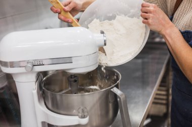 Hamur işi şefi blender için ahşap kaşık yardımıyla un döküyor.