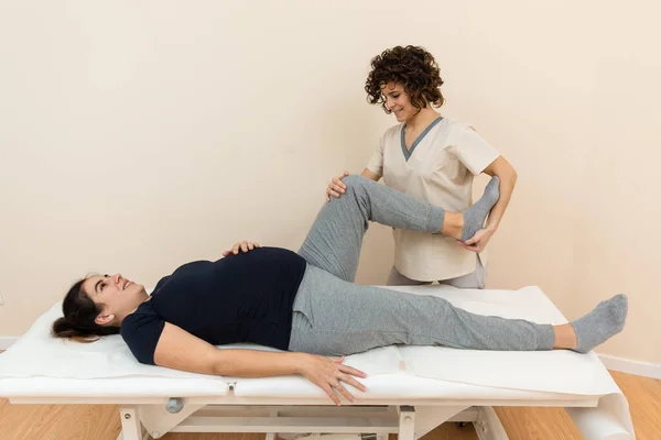 Una mujer embarazada acostada en una mesa de masaje mientras un fisioterapeuta se masajea las piernas en un centro de salud —  Fotos de Stock