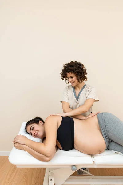 Fizioterapeuta masszírozza egy terhes nő hátát, aki az oldalán fekszik egy masszázsasztalon egy egészségügyi központban. — Stock Fotó