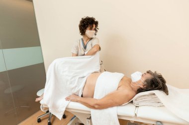 Fizyoterapist, havluları olan olgun bir kadına bacak masajı yapıyor.
