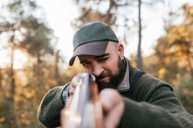 Tüfekli sakallı adam güneşli ormanda avlanıyor.