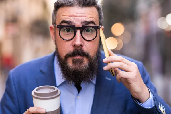 İş adamı telefonda konuşurken yüzünde şok edici bir ifadeyle kameraya bakıyor..