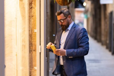 İş adamı sokakta dikilirken cep telefonunu kontrol ediyor..