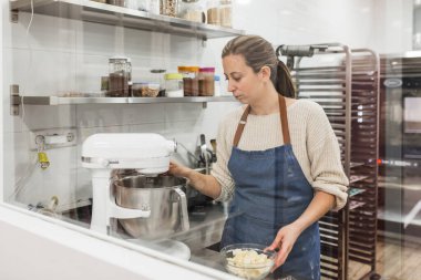 Kadın pasta şefi mutfakta yemek pişirmek için hamur hazırlarken elektrikli mikser kullanıyor..