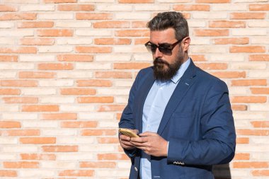 İş adamı, sokakta duvara karşı dururken cep telefonunu kullanıyor..