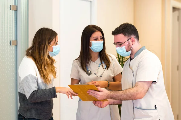 Dos doctores discutiendo notas en el portapapeles junto con una paciente en el centro médico —  Fotos de Stock