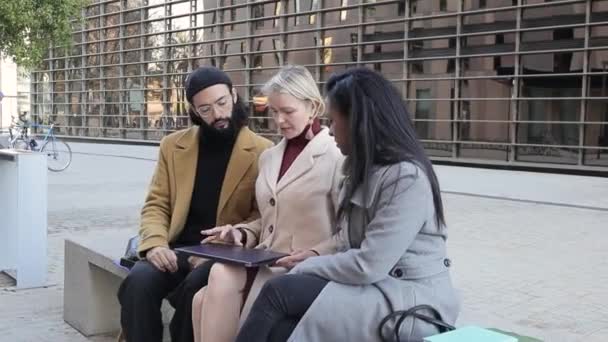 Business colleagues using a laptop while discussing business sitting on a bench in the street in the financial district. — ストック動画