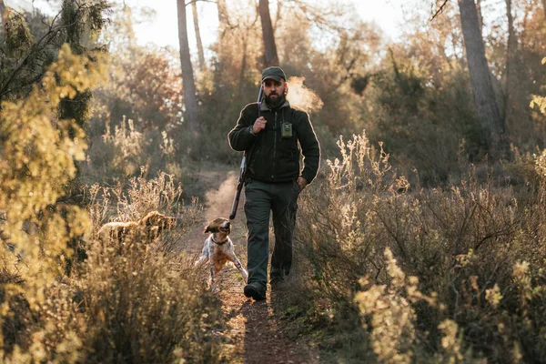 Man walking straight ahead carrying his gun with his dogs running around — Stock Photo, Image