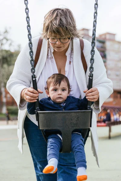 A mother playing with her little son in the swing in the playground — 스톡 사진