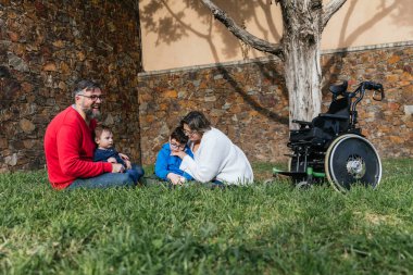 Parkta çimenlikte oturan mutlu bir aile günü birlikte geçiriyor.