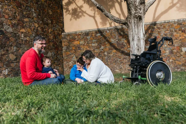 Parkta çimenlikte oturan mutlu bir aile günü birlikte geçiriyor.