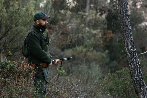 A fiatal vadász a vadászpuskáját a természet közepén tartja, és lenéz. — Stock Fotó
