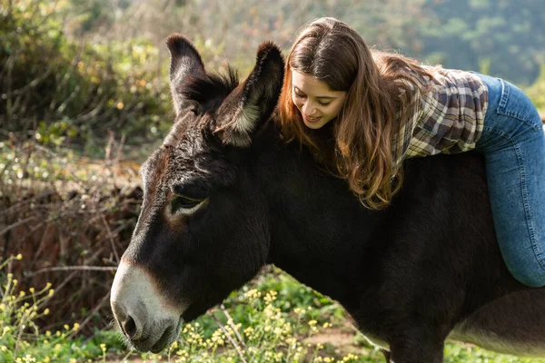 A happy young woman riding a donkey in the meadow — Photo