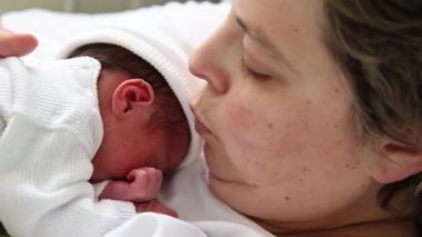 Mother kissing her newborn baby while he sleeping on her in the hospital room after the birth.
