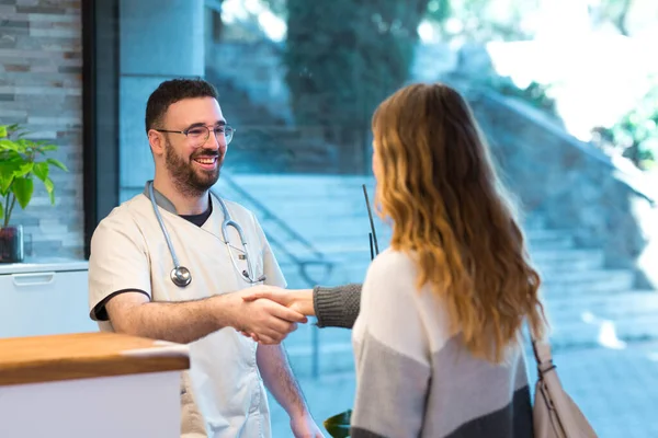 Male doctor and female patient greeting each other and shaking hands at the front desk reception. —  Fotos de Stock