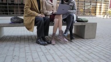 İş arkadaşları dışarıda bir bankta oturup yeni iş projelerini tartışırken dizüstü bilgisayar kullanıyorlar..