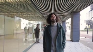 Finans bölgesinde ofis binasının önünde yürürken kameraya bakıp gülümseyen kendine güvenen bir işadamı..