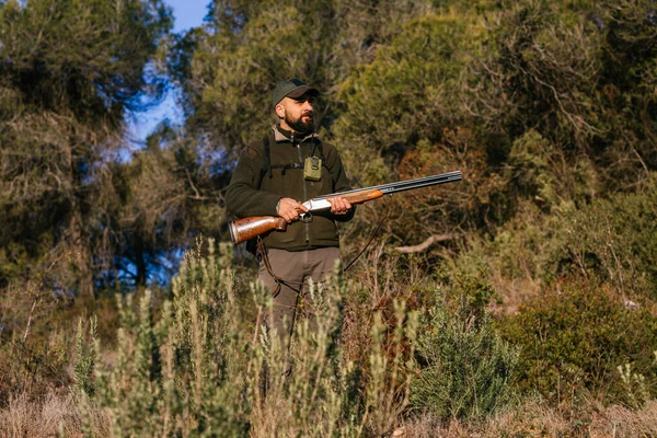Felnőtt férfi tartja a fegyverét a természet közepén, félrenéz. — Stock Fotó