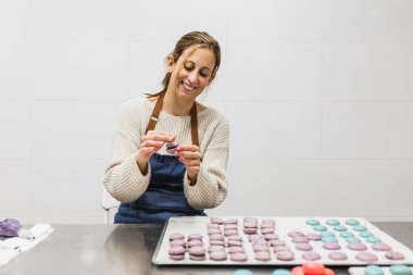 Pasta ya da pastanenin mutfağında renkli kurabiyeler hazırlarken gülümseyen kadın pasta şefi. Pasta ve fırın konsepti.