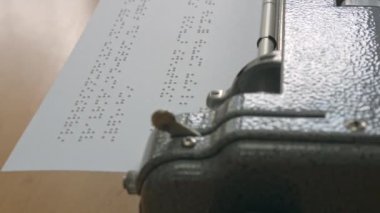 Eski Braille daktilo makinesinin Braille alfabesindeki harfleri kağıda kodlarken yakın çekim el kamerası görüntüsü. .