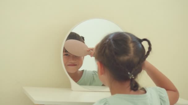Азиатская Маленькая Девочка Расчесывает Волосы Чёлкой Улыбается Зеркале Туалетного Столика — стоковое видео