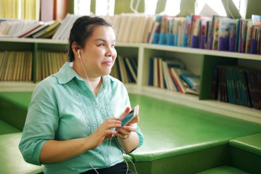 Portrait of Asian woman with blindness disability enjoy using smart phone with voice accessibility for persons with visual impairment in creative workplace library.