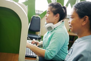 Asian woman with blindness disability using computer keyboard and braille display assistive device working with senior colleague woman in office workplace.