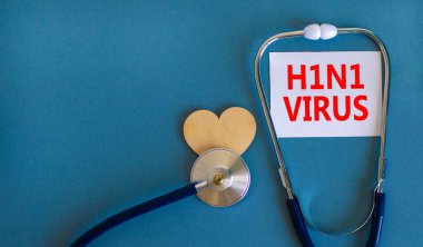 H1N1 virüs sembolü. Üzerinde H1N1 virüsü yazan beyaz kart, güzel mavi arka plan, tahta kalp ve stetoskop. Tıbbi, H1N1 virüs konsepti.