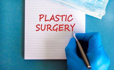 Plastik cerrahi sembolü. Plastik cerrahi, güzel mavi arkaplan, doktor eli mavi eldiven ve metalik kalem içeren beyaz bir not. Tıbbi maske. Tıbbi ve plastik cerrahi konsepti.