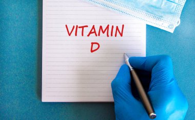 D vitamini sembolü. D vitamini, güzel mavi arkaplan, doktor eli mavi eldiven ve metalik kalem içeren beyaz bir not. Tıbbi maske. Tıbbi, D vitamini konsepti.