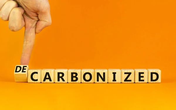 炭素化または脱炭素化シンボル ビジネスマンは木製の立方体を回転させ 炭素化 という言葉を 脱炭素化 に変えます オレンジの背景 コピースペース 炭素化又は脱炭素化の概念 — ストック写真