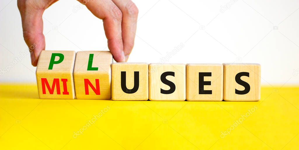 Pluses and minuses symbol. Businessman turns wooden cubes and changes the word 'minuses' to 'pluses'. Beautiful yellow table, white background. Business, pluses and minuses concept, copy space.