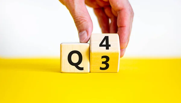 Üçüncü çeyrekten dördüncü çeyreğe kadar. İşadamı tahta küpü döndürür ve 'Q3' kelimesini 'Q4' e çevirir. Güzel sarı masa, beyaz arka plan. İş dünyası, mutlu 4. çeyrek kavramı, kopyalama alanı.