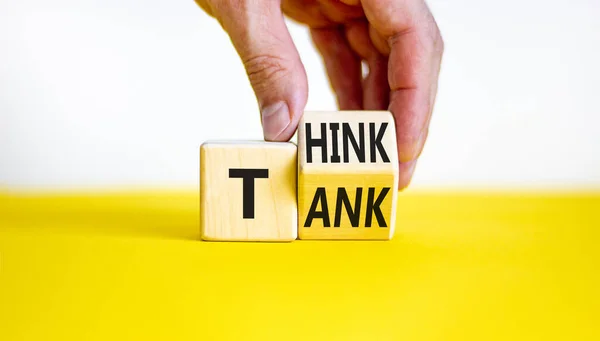 Think tank symbol. Businessman turns a wooden cube and changes the word \'tank\' to \'think\' or vice versa. Beautiful yellow table, white background, copy space. Business, think tank concept.