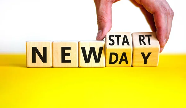 New day and start symbol. Businessman turns wooden cubes and changes words \'new day\' to \'new start\'. Beautiful yellow table, white background. Copy space. Business, new day and start concept.