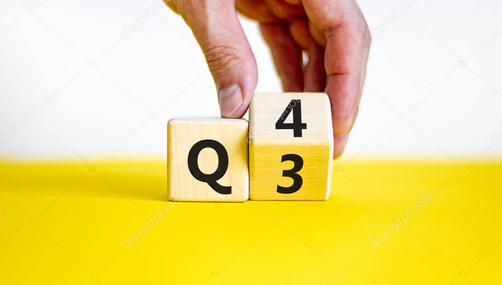 From 3rd to 4th quarter symbol. Businessman turns a wooden cube and changes words 'Q3' to 'Q4'. Beautiful yellow table, white background. Business, happy 4th quarter Q4 concept, copy space.